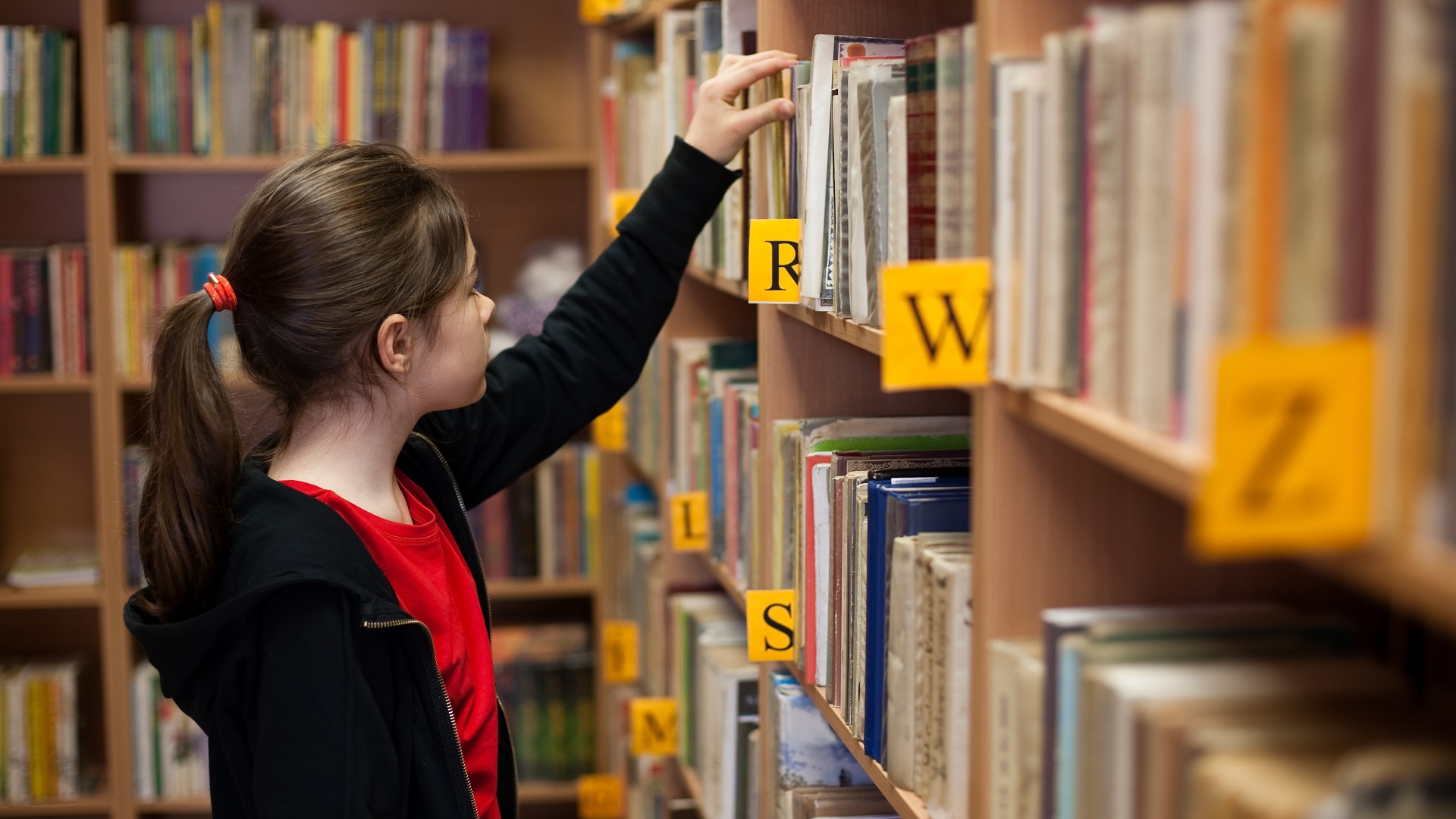 A Check-In On My "To Read" List girl in library picking out book